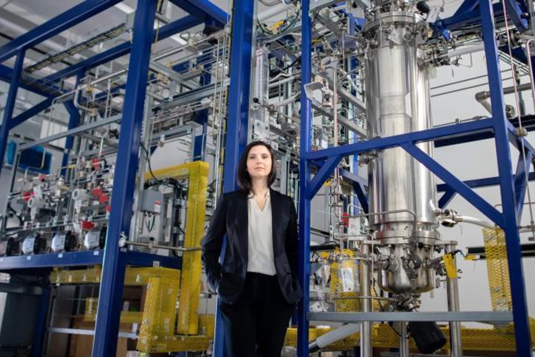 Circe Bioscience founder Shannon Nangle stands in front of a complex system of steel pipes and reactors.