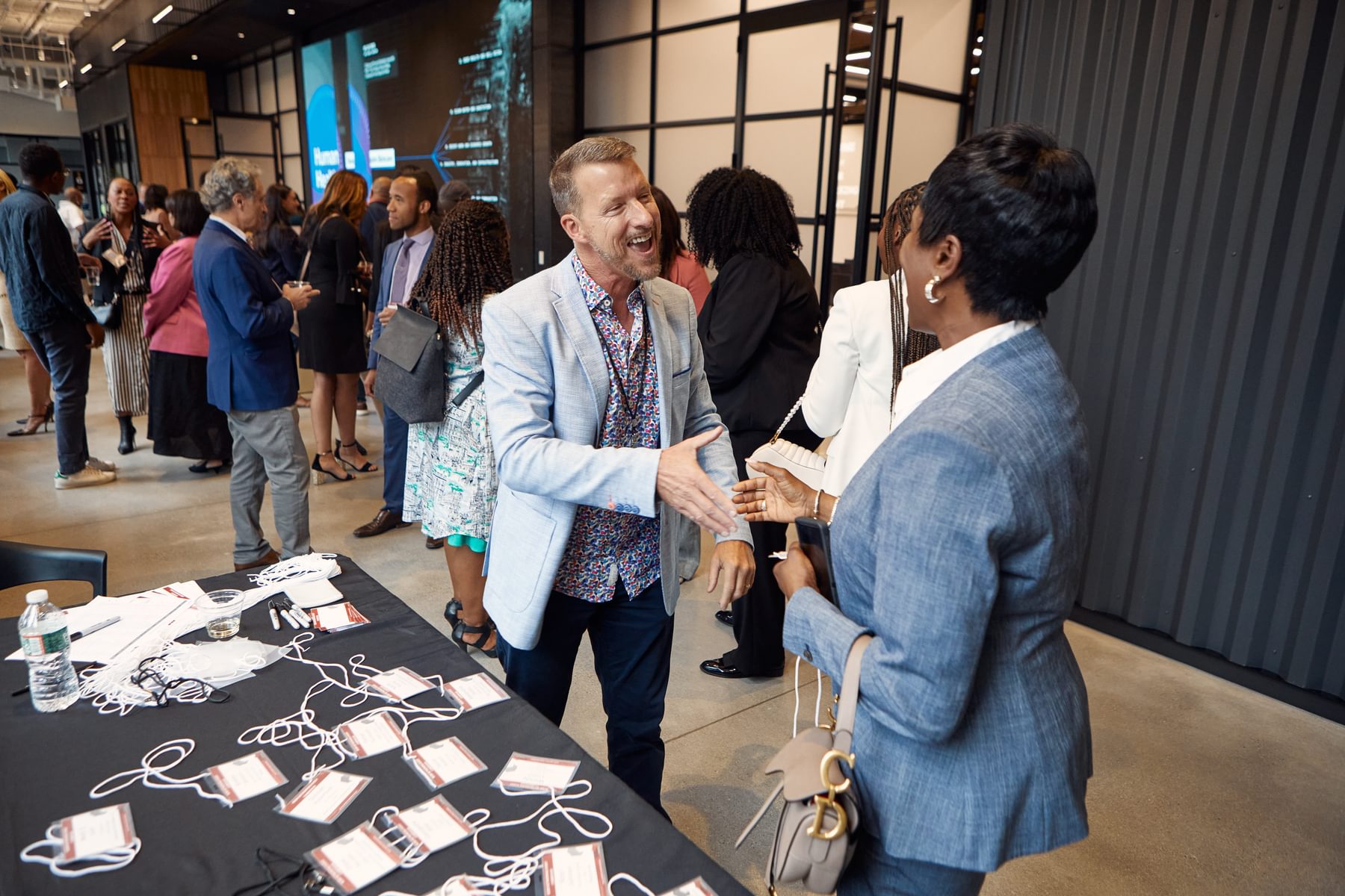 A man shakes hands with a woman in front of a name tag booth at Tough Tech Week 2024.