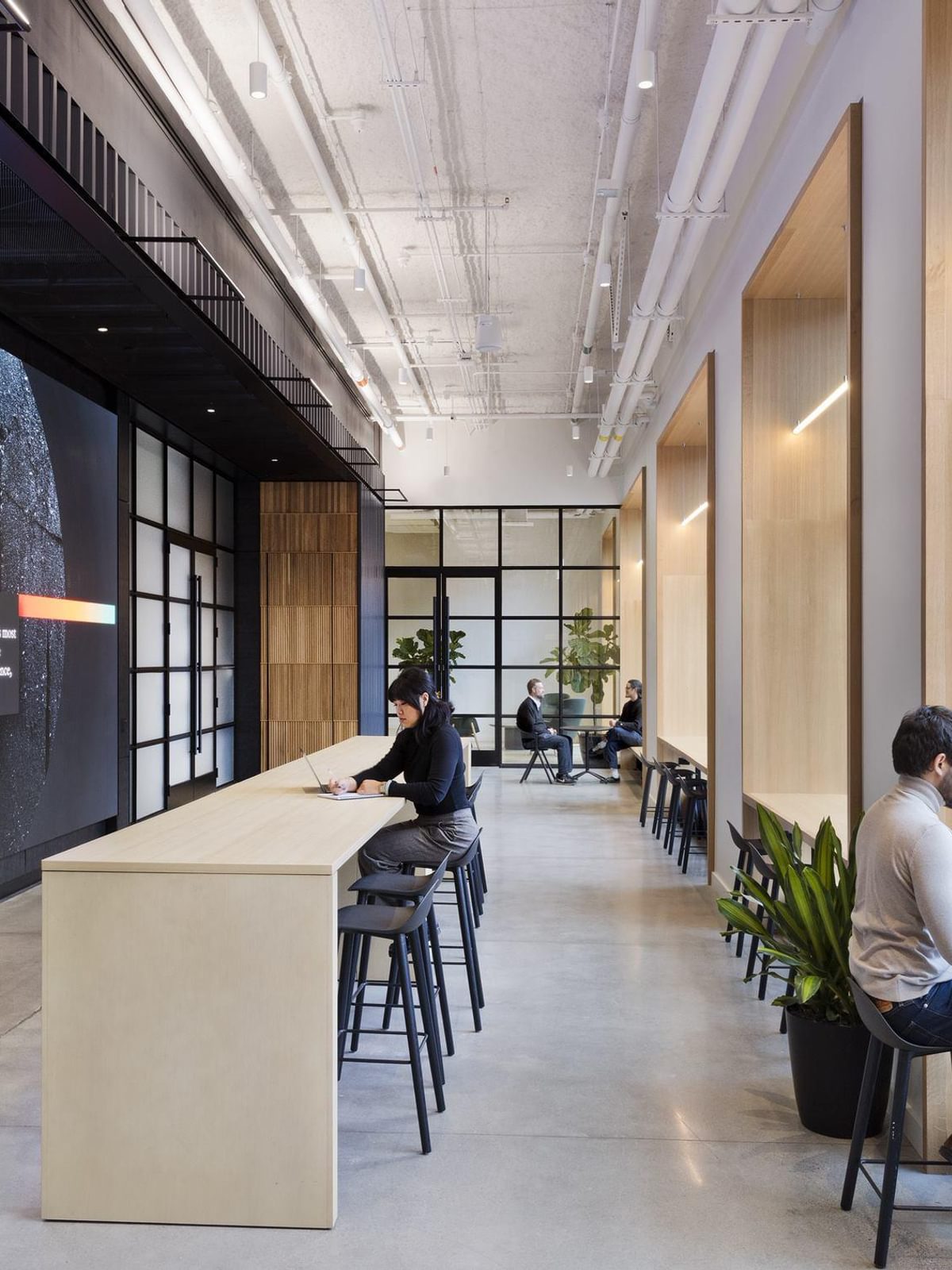 A view of the first floor of The Engine, featuring a large display on the wall and residents working and meeting at the available desks.
